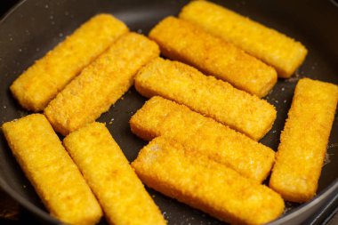 Fish sticks in a pan. Preparation of frozen fish sticks. Fast food.