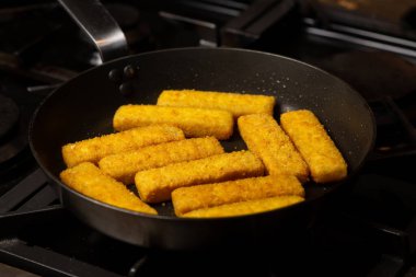 Fish sticks in a pan. Preparation of frozen fish sticks. Fast food.