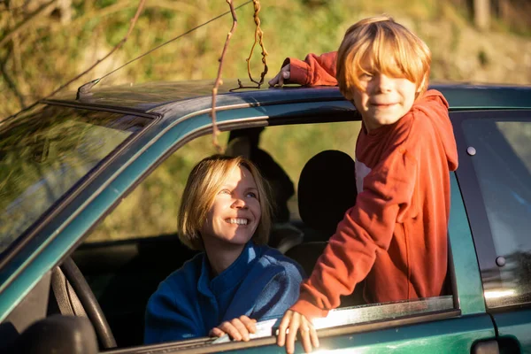 A mother and son, a young boy, smile in a car at a rest stop. A trip with a child by car, a halt. Automobile travel.