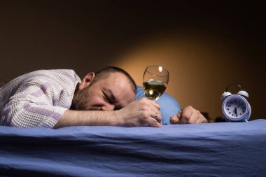 A man alone with a glass of wine in bed. Alcoholism, loneliness. Drink alcohol to sleep. A dark room.