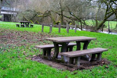 Empty benches with tables for tourists to rest on the green grass near the river. A place of rest for tourists and travelers.