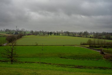 View of the green meadows in cloudy weather. Fields and roads in a rural hilly area.