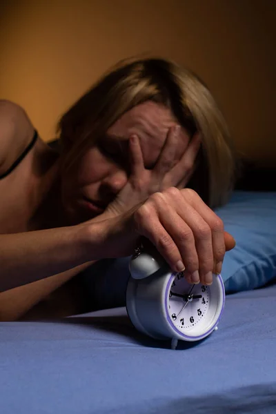 Irritation of a woman in the morning from the alarm clock. Poor sleep, violation of the regimen, lack of sleep concept. A middle-aged woman turns off the alarm clock.