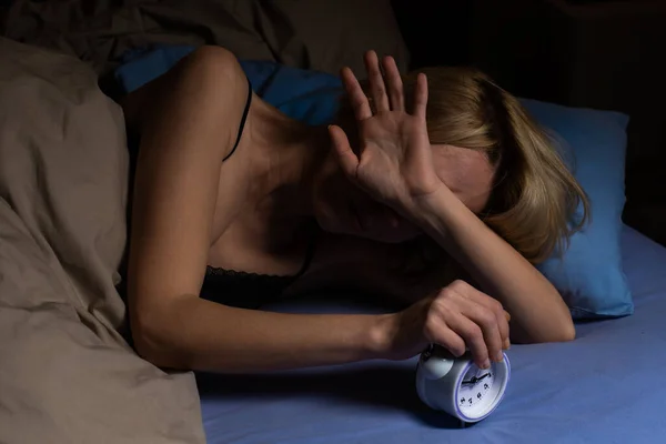 The woman nervously wakes up from the alarm clock. Poor sleep, violation of the regimen, lack of sleep concept. A middle-aged woman turns off the alarm clock.