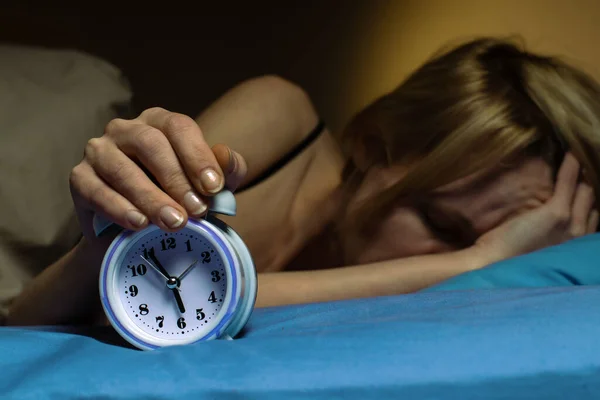 The woman cannot wake up in the morning. Poor sleep, violation of the regimen, lack of sleep concept. A middle-aged woman turns off the alarm clock.
