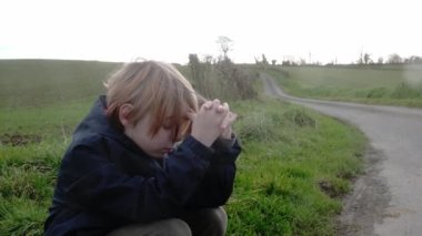 Portrait of a young boy of nine years old who is squatting on the green grass. Tiredness, exhaustion from a long walk. Restoration of forces.