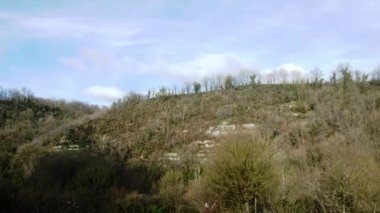 View of a high hill or mountain covered with green vegetation and trees. Sky with small clouds, plain. Countryside in France.