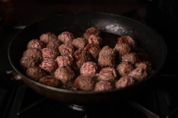 Cooking delicious homemade beef meatballs in a frying pan. Dark background. Meat balls.