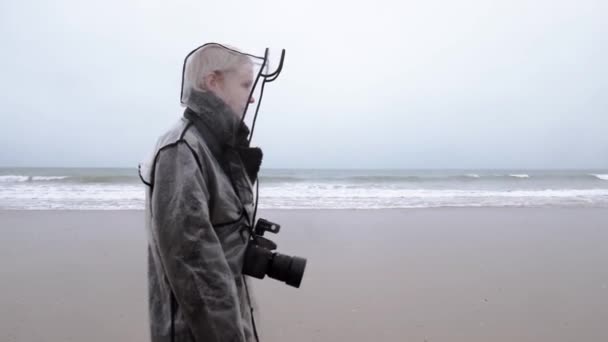 一个女人带着相机沿着大海的海岸走着 一位中年妇女在雨中拍照 — 图库视频影像