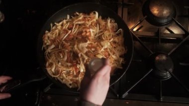 Cooking stewed cabbage. An unrecognizable person adds salt to a frying pan in which cabbage and carrots are fried. Top view.