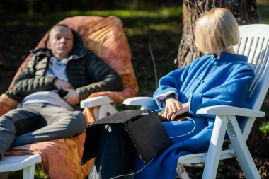A portable solar panel rests on the legs of a woman talking to a man. Camping. Ecological alternative energy concept.