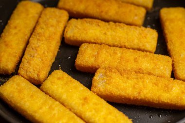 Fish sticks in a pan. Preparation of frozen fish sticks. Fast food.