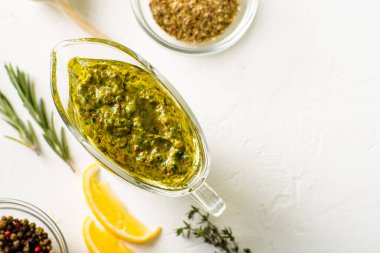 Beyaz arka planda soslu Chimichurri sosu. Yakınlarda çeşitli baharatlar var. Zeytin yağı, kekik otu ve maydanozdan yapılmış Arjantin vejetaryen sosu. Metin için yer.