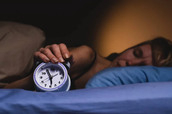The woman nervously wakes up from the alarm clock. Poor sleep, violation of the regimen, lack of sleep concept. A middle-aged woman turns off the alarm clock.