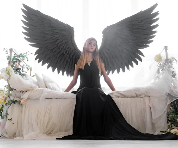 Ангел Чорними Крилами Білому Ліжку Квітах Молода Вдумлива Дівчина Сидить — стокове фото