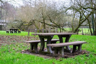 Empty benches with tables for tourists to rest on the green grass near the river. A place of rest for tourists and travelers.