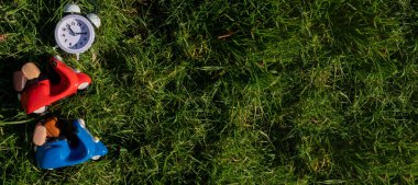 Scooter 'la seyahat zamanı, hızlı teslimat konsepti. İki oyuncak scooter ve yeşil çimlerde çalar saat. Pankart, metin için boşluk