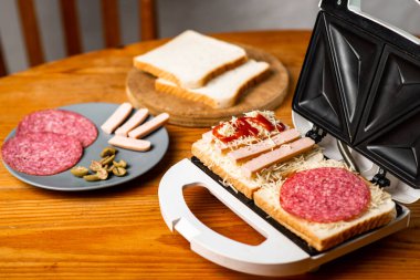 Sandviç makinesi ve sandviç yapma. Farklı malzemeler ahşap masada yan yana yatar..