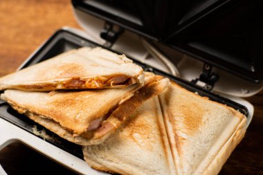 Tahta bir arka planda sandviç makinesinde yeni yapılmış tost sandviçler. Peynirli üç köşeli sandviç..