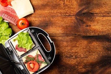 Farklı dolgularla sandviç pişirmek. Sandviç makinesi ve ahşap arka planda çeşitli malzemeler. Metin için yer.