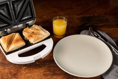 Kızarmış sandviçler, boş bir tabak ve ahşap arka planda bir bardak portakal suyu. Hafif sabah kahvaltısı, atıştırmalık.