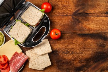 Farklı dolgularla sandviç pişirmek. Sandviç makinesi ve ahşap arka planda çeşitli malzemeler. Metin için yer.