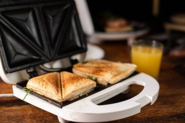 Tahta bir arka planda sandviç makinesinde taze hazırlanmış sandviçler..