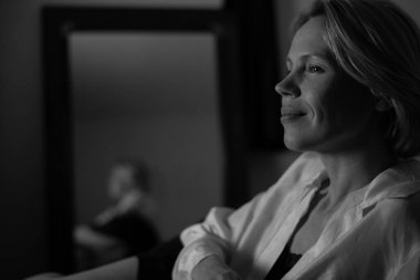 Hoş düşünceli bir kadın. Orta yaşlı bir kadın gülümseyerek yüzünü çevirir. Sakin, huzurlu atmosfer, dinlenme ve rahatlama. siyah beyaz fotoğraf.