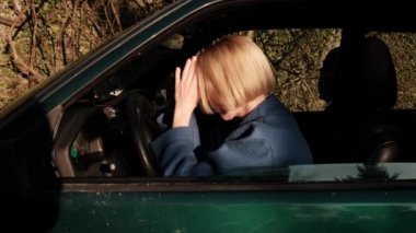Tired woman driving a car. A woman with her hands folded in prayer. Loss of strength, emotional devastation. View from outside the car.