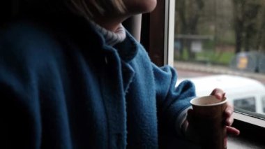 Rotterdam, Hollanda - 10 Mart 2023: Bir kadın apartmanın penceresinin yanındaki karton bardaktan kahve içiyor.