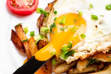 Yumurtalı kızarmış patates, sıvı sarısı, otlar ve domatesler beyaz tabakta..