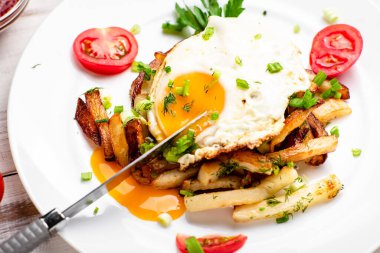 Yumurtalı kızarmış patates, sıvı sarısı, otlar ve domatesler beyaz tabakta..