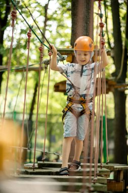 Çocuklar için ip parkı. Kanatlı genç bir çocuk engellere tırmanıyor. Çocuğun aktif spor eğlencesi.