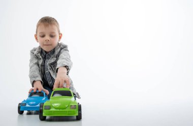 Genç bir çocuk beyaz arka planda çok renkli oyuncak arabalarla oynuyor. Çocuk eğlencesi, eğlence..