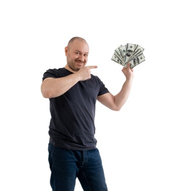 Kotlu ve tişörtlü tatmin olmuş bir adam dolarları tutar ve parmaklarıyla onları işaret eder. Beyaz arka planda izole edilmiş. Kâr, servet, piyango konseptini kazanmak..