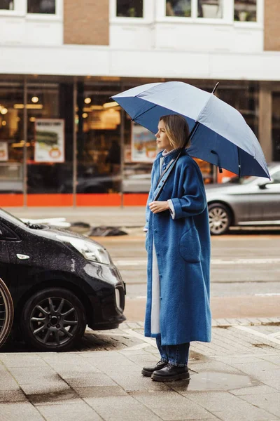 Woman with an umbrella in the city. Blue coat and blue umbrella. Middle-aged tourist woman smiling.