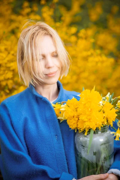Een Vrouw Een Blauwe Jas Een Gele Achtergrond Van Bloemen — Stockfoto