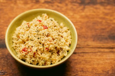 salad of couscous, spices and tomato tabbouleh in a yellow plate on a wooden background.