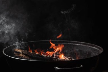 Firewood burns in a round barbecue at night. Dark background. Preparing to cook food on the grill.