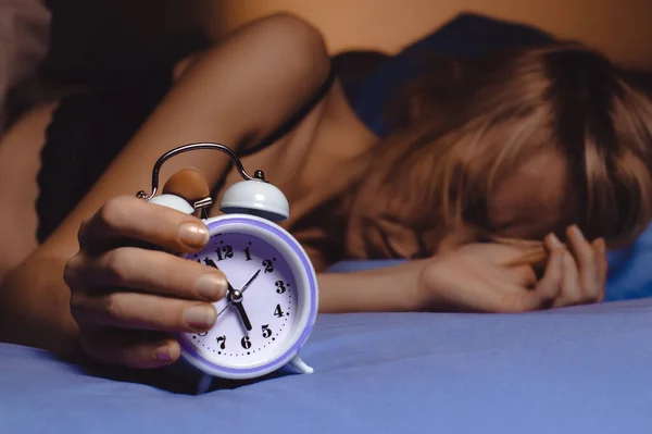 The woman cannot wake up in the morning. Poor sleep, violation of the regimen, lack of sleep concept. A middle-aged woman turns off the alarm clock.
