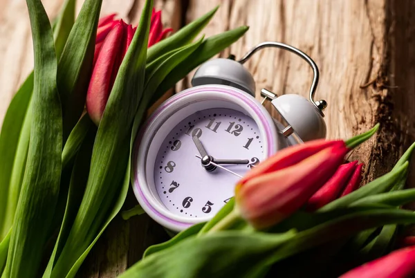 stock image Alarm clock in tulip flowers on wooden background. Concept of time as gift, congratulations, onset of spring.