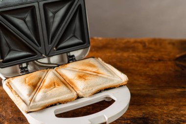 Tahta bir arka planda sandviç makinesinde yeni yapılmış tost sandviçler. Sabah kahvaltısı kavramı.