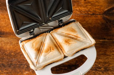 Tahta bir arka planda sandviç makinesinde yeni yapılmış tost sandviçler. Sabah kahvaltısı kavramı.