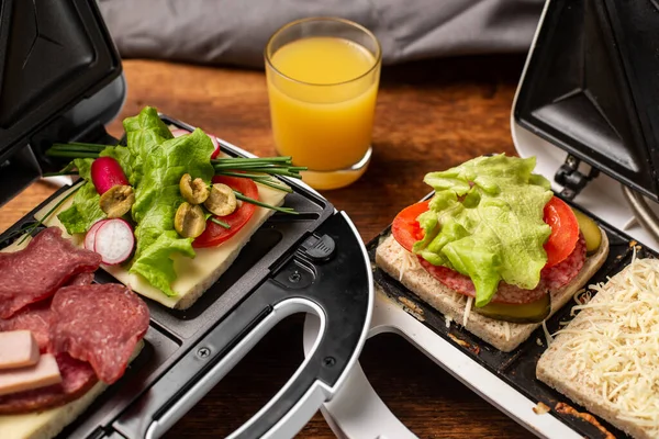 Stock image Different types of sandwiches in a sandwich maker on a wooden background with different ingredients and a glass of orange juice. Place for text.