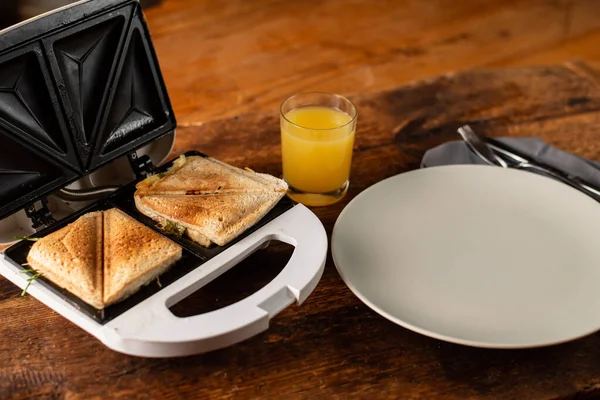 stock image Toasted sandwiches on a toast sandwich, an empty plate and a glass of orange juice on a wooden background. Light morning breakfast, snack.