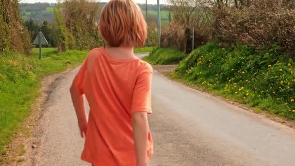那男孩沿着大路走着 有趣的愚蠢的散步 农村一个穿着橙色T恤的男孩 徒步旅行 学校假期 — 图库视频影像
