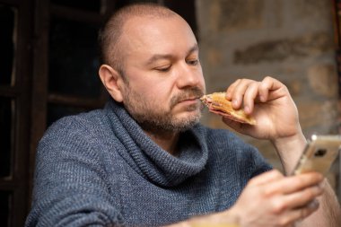 Bir adam sandviç yer ve evdeki telefona bakar. Sıradan orta yaşlı bir adam. Elinde telefonla yemek yiyorsun..