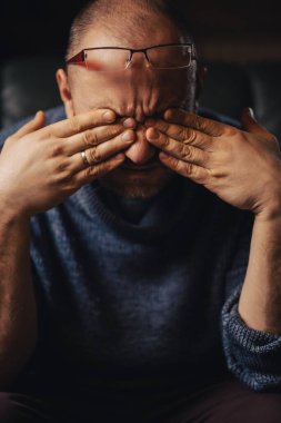 Bir adam bir kitabın önünde gözlerini ovuşturur. Gözlerde ağrı, yorgunluk, baş ağrısı..