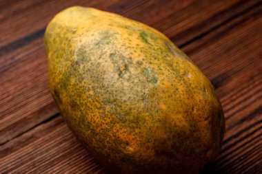Ahşap bir arka planda bütün papaya. Düz olmayan yüzeyi olan kusurlu görünümlü bir meyve..
