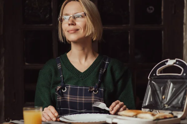 女性はサンドイッチメーカーとプレートとテーブルに座っています 中年女性 適切な栄養 — ストック写真